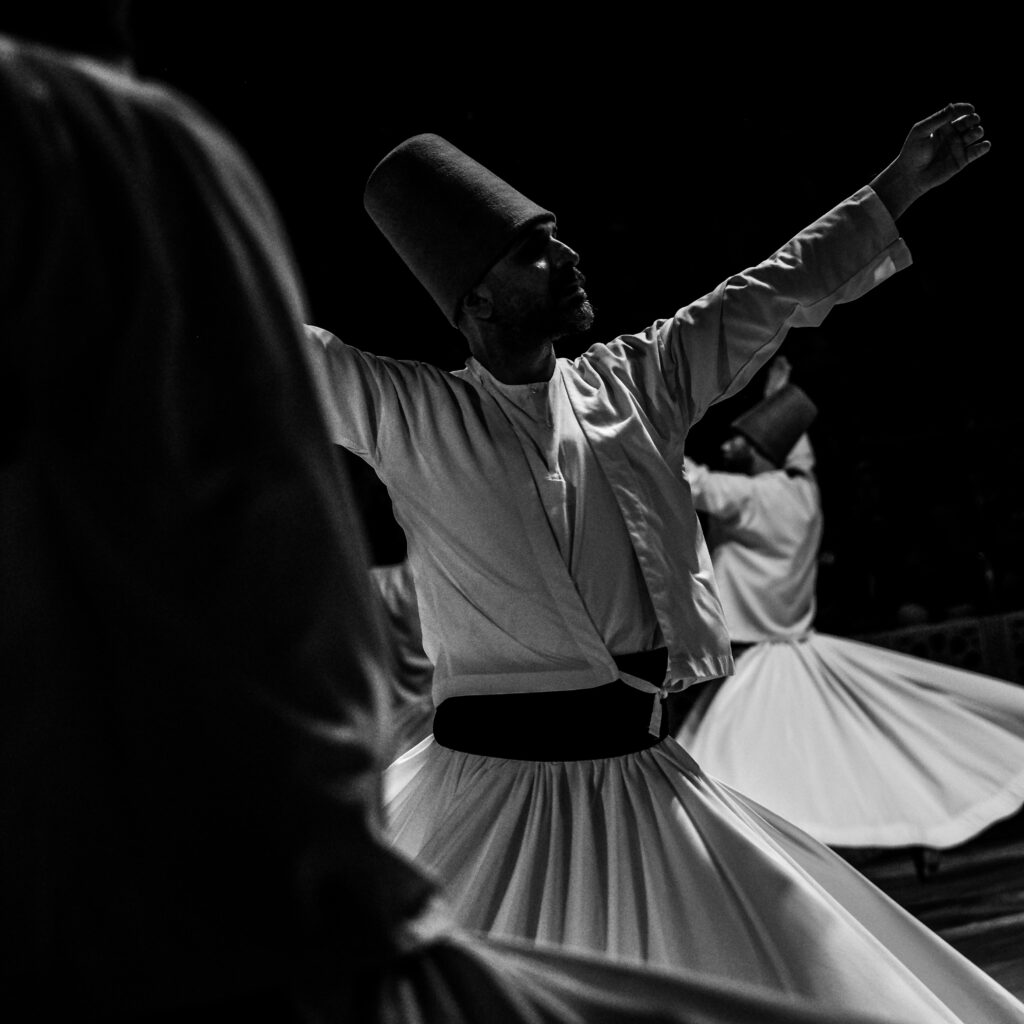 Black and white photograph capturing Sufi dancers in traditional whirling rituals in Konya, Türkiye.